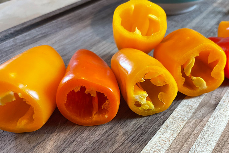 peppers on a wooden chopping board with the tops cut off and seeds removed