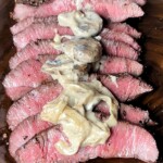 grilled flat iron steak sliced topped with mushroom sauce on a wooden board