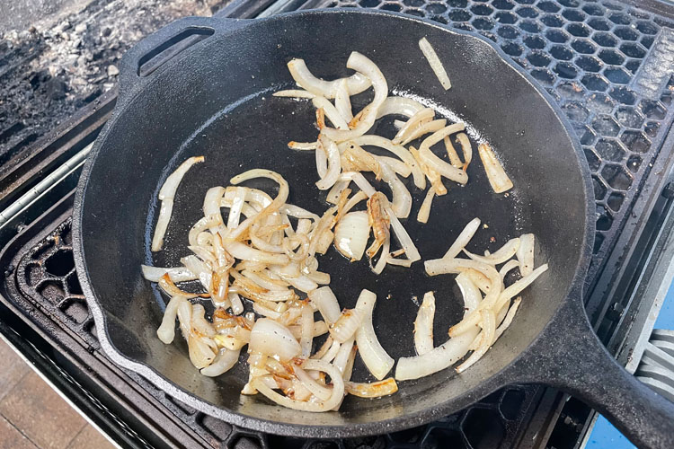 sliced onions cooking in a cast iron skillet on a grill