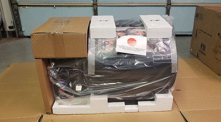 Camp Chef DLX 24 pellet grill packaged in a plastic wrap and cardboard