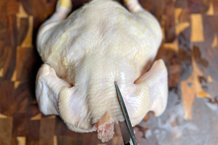 raw chicken on wooden board with scissors cutting the backbone