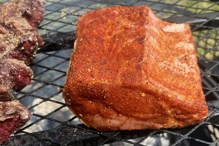 seasoned rack of pork on the grill skin side down