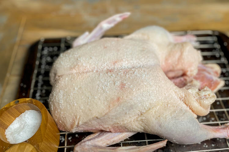 raw duck covered in kosher salt on a wire rack