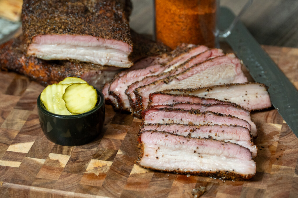 a board with sliced pork belly and a bowl of pickles, all ready to eat