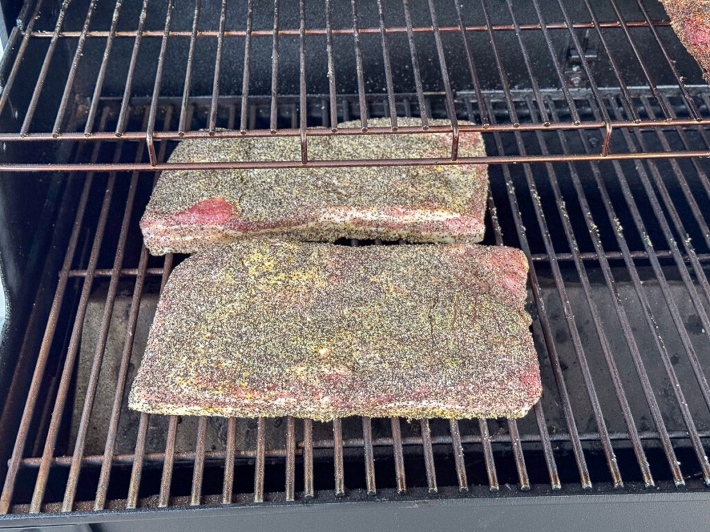 raw seasoned pork belly slabs on the smoker