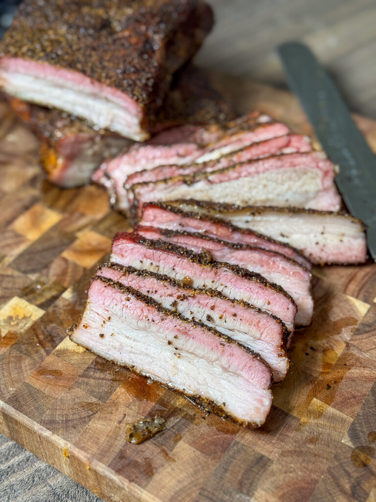 smoked pork belly sliced up displayed on a wooden chopping board