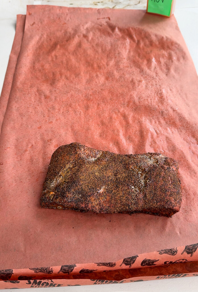 a cooked piece of pork belly on pink butcher paper waiting to be wrapped