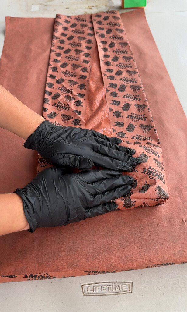 black gloved hands wrapping pork belly in pink buther paper