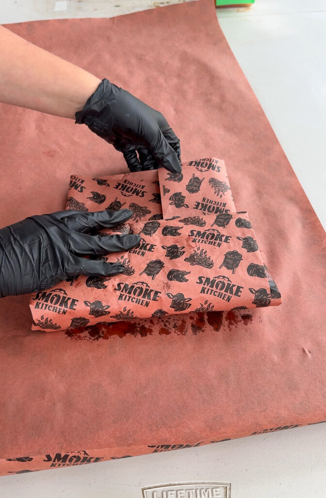 black gloved hands wrapping pork belly in pink butcher paper
