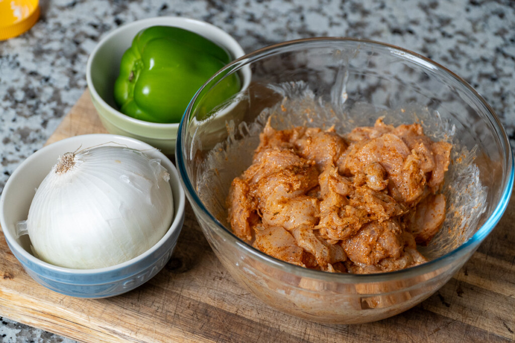 raw marinated chicken in a glass bowl with an onion and green capsicum in bowls on the side