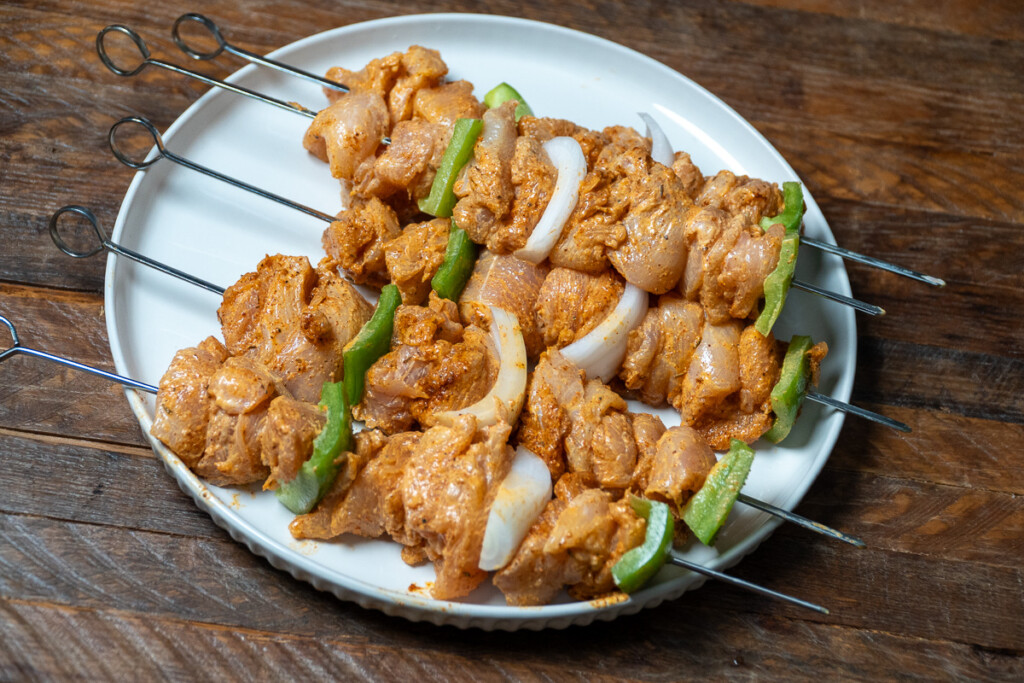 four skewers of raw marinated chicken on a white plate
