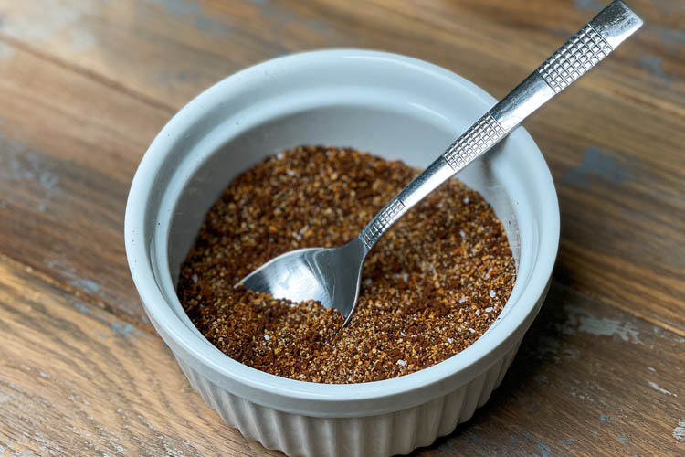 white bowl with coffee rub and a teaspoon in it on a wooden board