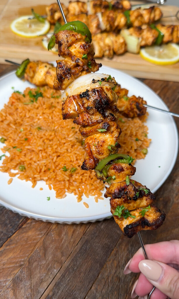 a skewer of cooked chicken in frontof a plate of mexican rice