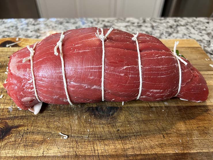 rolled stuffed flank steak on a wooden board