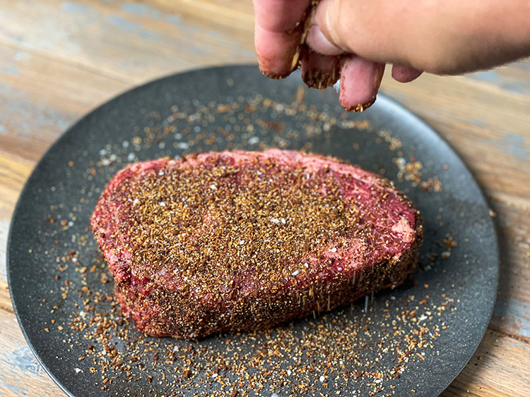 Hand sprinkling coffee rub on raw ribeye steak