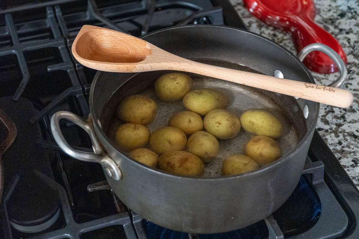 raw potatoes in a pot of water on the hob with a wooden spoon resting on top of the pot