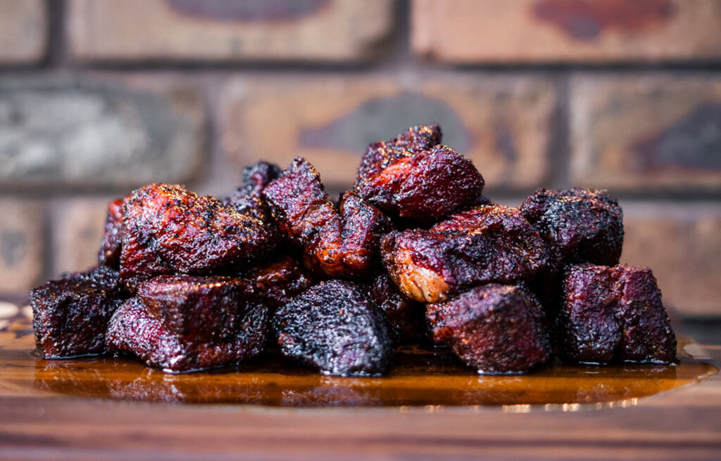 Smoked poor man’s burnt ends made from beef chuck roast, stacked on a wooden board with a dark bark and juicy interior.