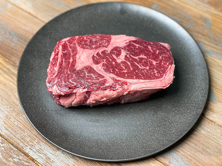 raw ribeye steak on black plate