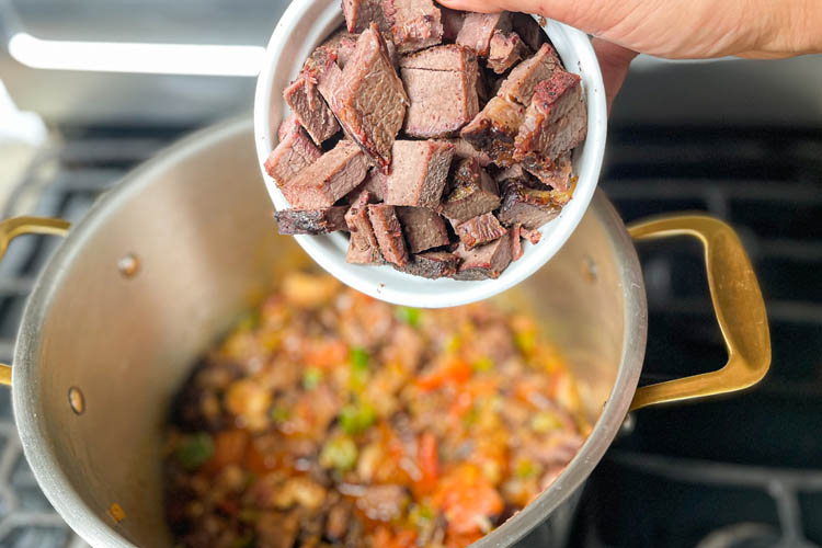 pot with sauted veges in the background, bowl of brisket chunks in foreground