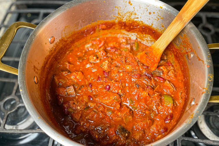cooked brisket chili in a silver pot with a wooden spoon in it