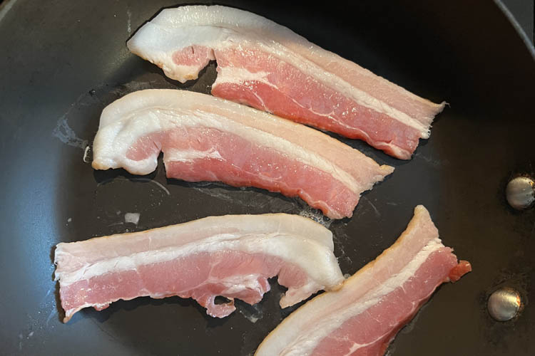 four bacon slices cooking in a frypan