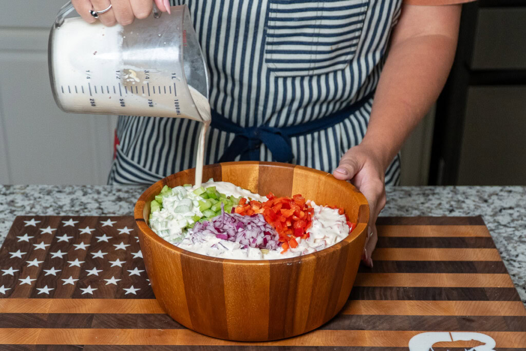 a jug of salad dressing being poured over macaroni salad