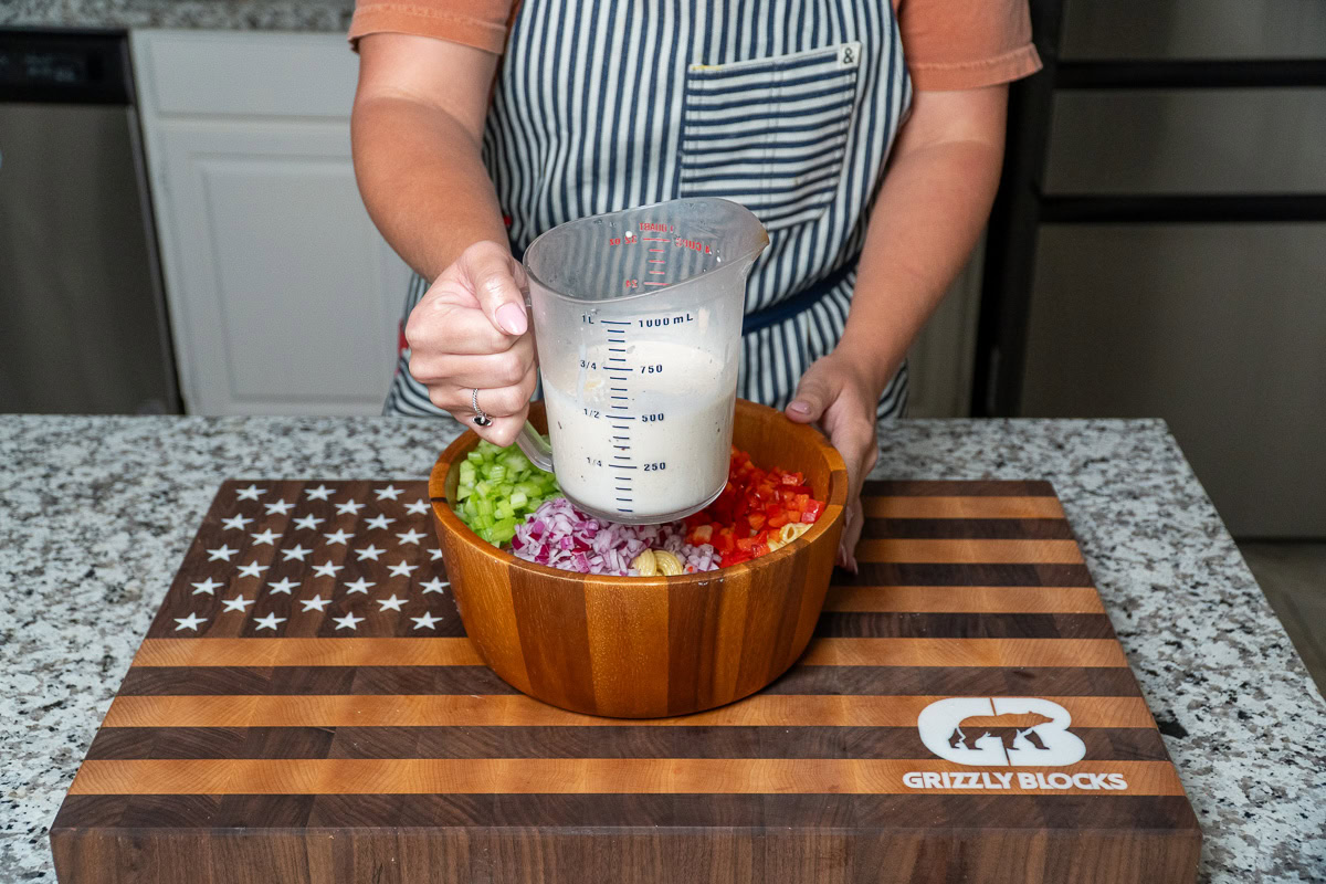 a jug of macaroni pasta salad dressing over a bowl of salad sans dressing