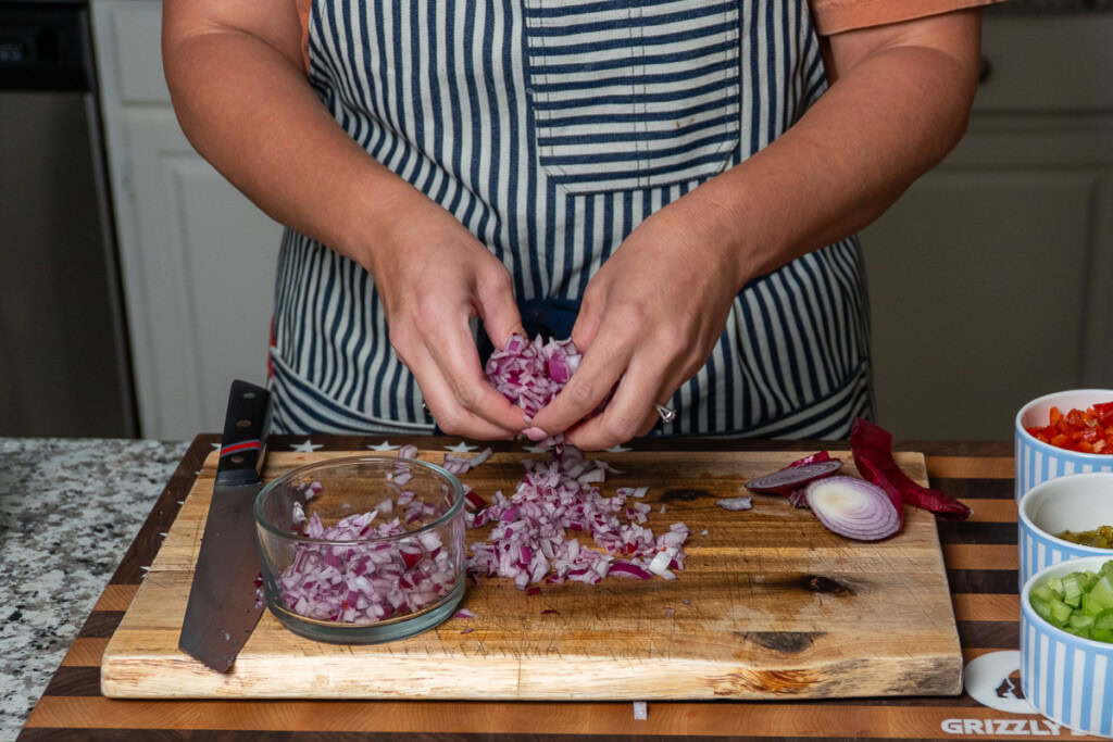 a person putting diced red onion into a prep bowl