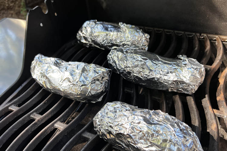 four potatoes wrapped in foil on the grill