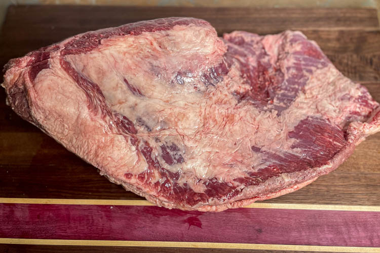 bottom side of raw brisket on wooden chopping board