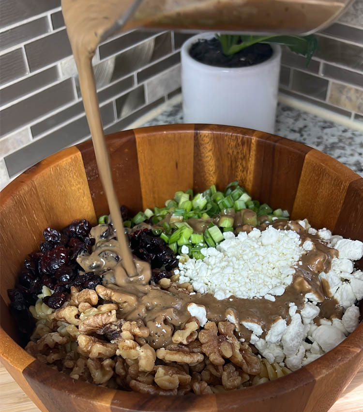 dressing begin poured over pasta salad