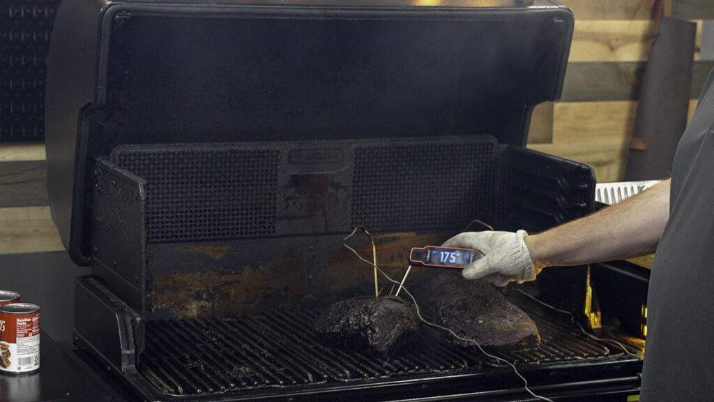 person wearing a heat-resistant glove checks the internal temperature of a smoked brisket on a pellet grill using a digital meat thermometer, which reads 175°F.
