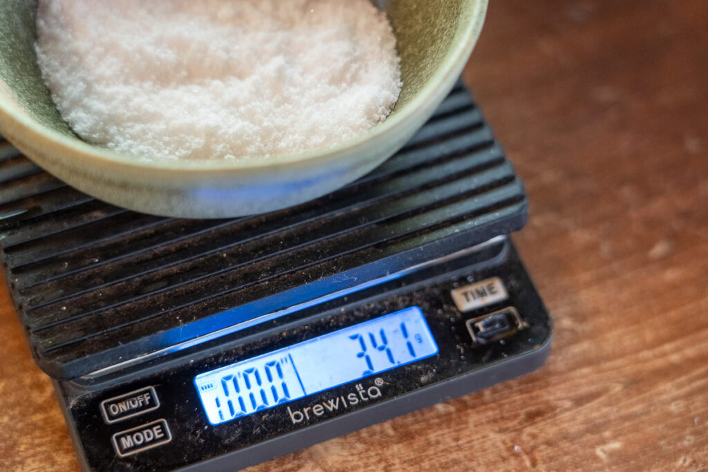Kosher salt measured precisely on a digital kitchen scale, showing a weight of 34.1 grams for bacon curing.