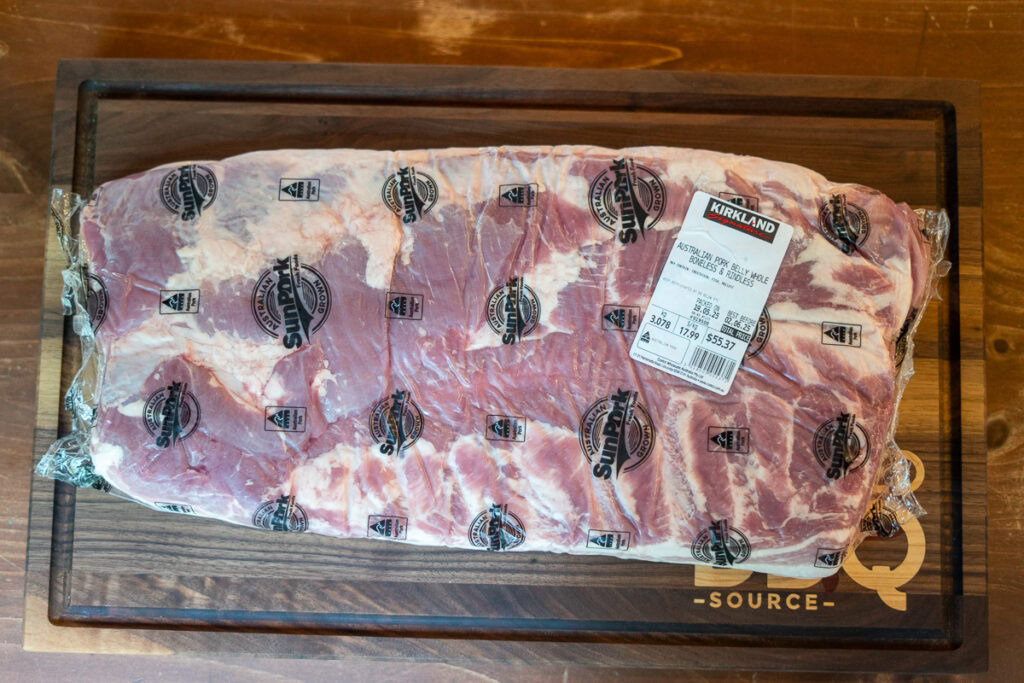 Vacuum-sealed whole pork belly in original Kirkland packaging from Costco, placed on a cutting board before curing.