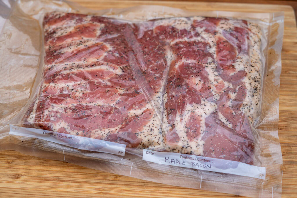 Vacuum-sealed pork belly labeled “Maple Bacon” after curing, ready for smoking.