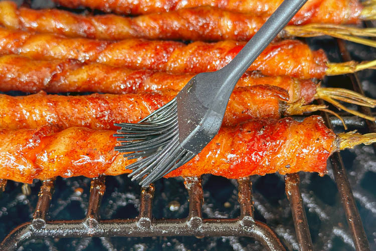 bacon wrapped carrot being brushed with glaze with black brush