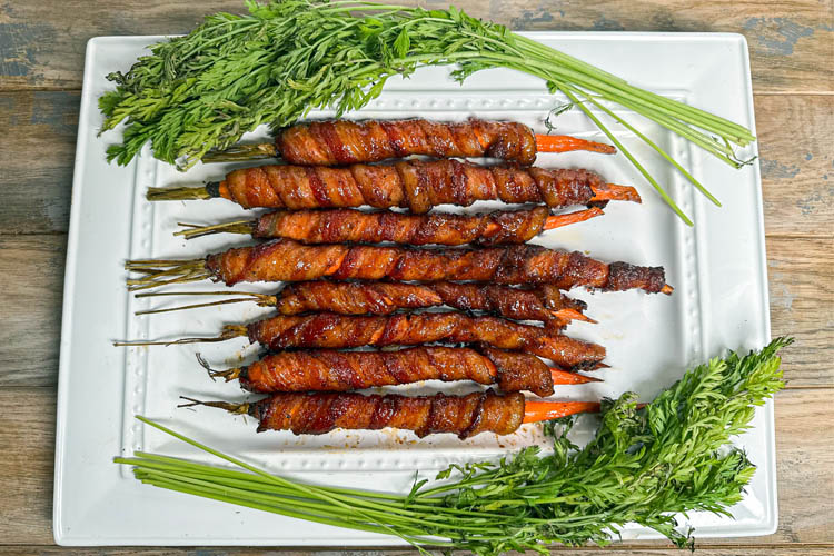 plated bacon wrapped carrots with carrot top greenery on a white plate