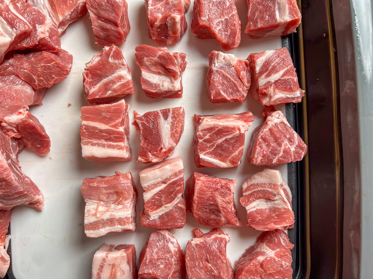 Cubed pork butt pieces on a cutting board, ready for seasoning.