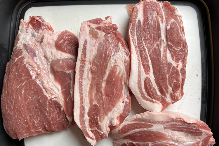 slices of raw pork butt on a white chopping board