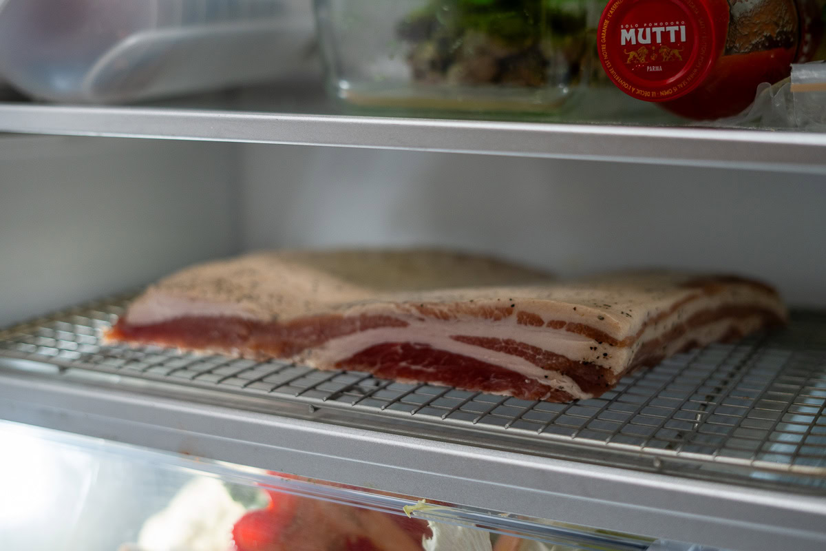 Cured pork belly resting on a wire rack in the refrigerator, uncovered, to develop a pellicle before smoking.