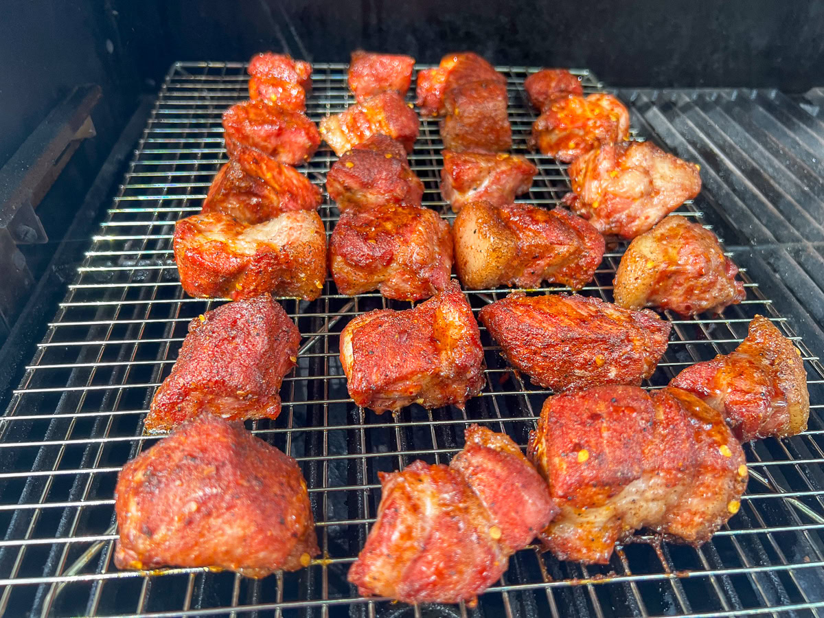 Seasoned pork butt cubes arranged on a wire rack inside a smoker.