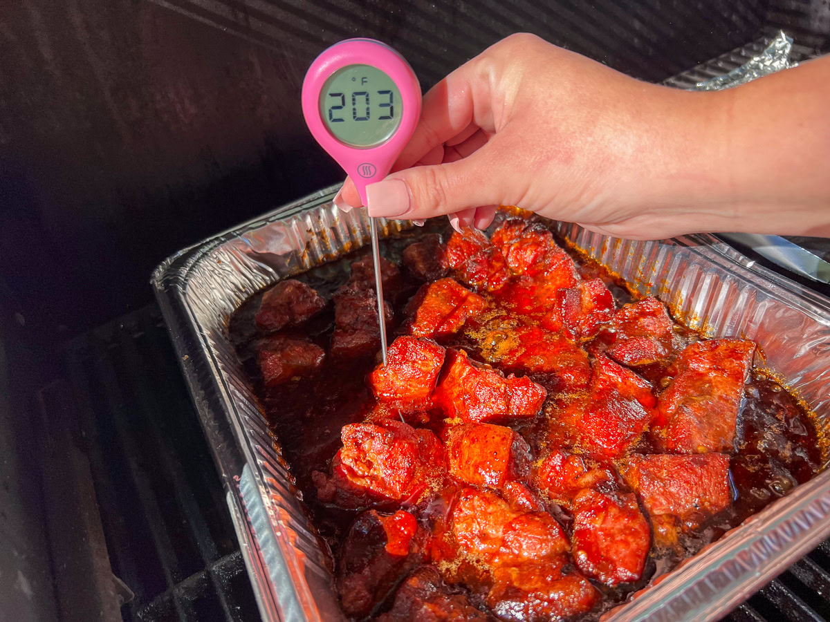 Glazed pork burnt ends uncovered in a smoker, bubbling in sauce.