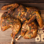 Smoked spatchcock turkey on a wooden board with crisp skin and herb seasoning.