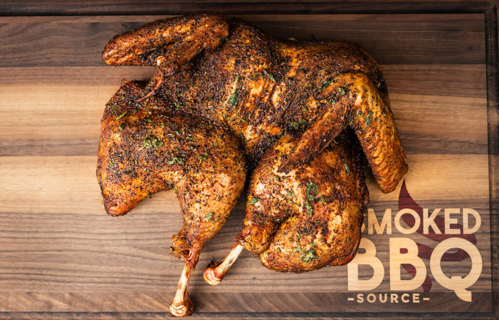 Whole smoked spatchcock turkey on a cutting board showing even browning and herb rub