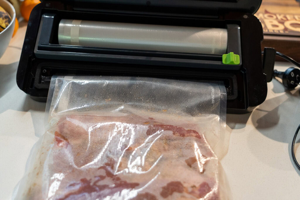 Vacuum sealer packaging a slab of pork belly in a plastic bag during the curing process for homemade bacon.