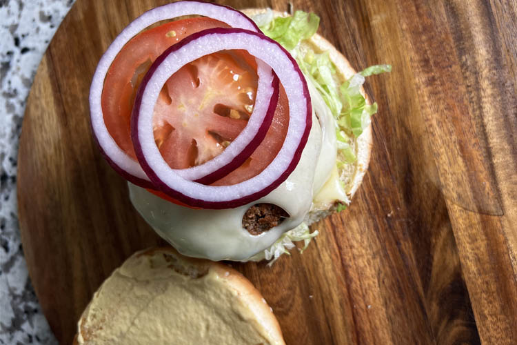 burger bun with lettuce, patty, cheese, tomato and onion rings on a wooden board