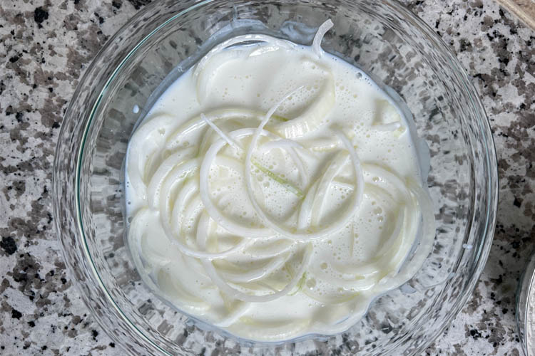 sliced onions in a bowl of buttermilk
