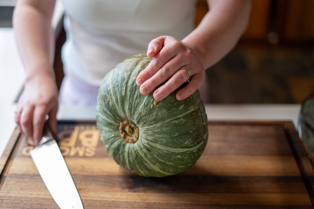 cutting a raw pumpkin in half before smoking for pumpkin pie filling