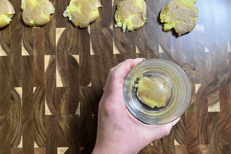 hand holding a glass that is squashing a cooked potato