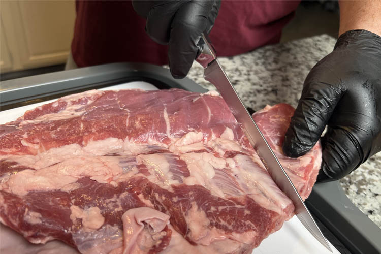 hand cutting the end flap off a rack of pork ribs